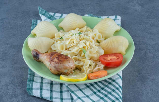 Plate of boiled pasta and chicken drumstick on stone surface. 