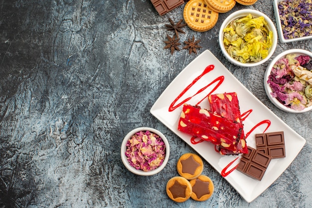 Free photo a plate of chocolate with cookies and dry flowers around it on grey