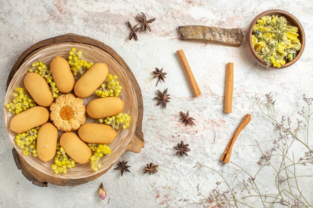 A plate of cookies on wooden platter and different dry herbs around it on marble