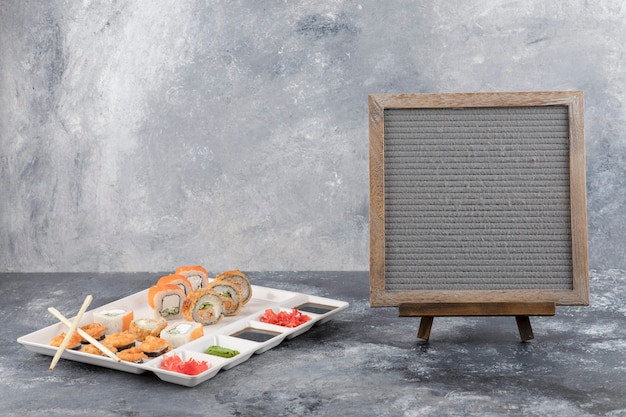 Free Photo plate of delicious sushi rolls and wooden frame on marble background