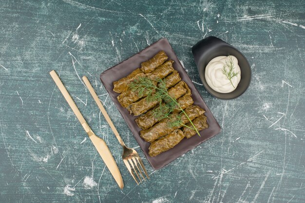 Plate of dolma and sour cream on marble surface .