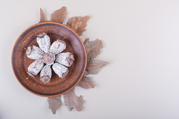 Plate of dried persimmons and dry leaves on white background. High quality photo