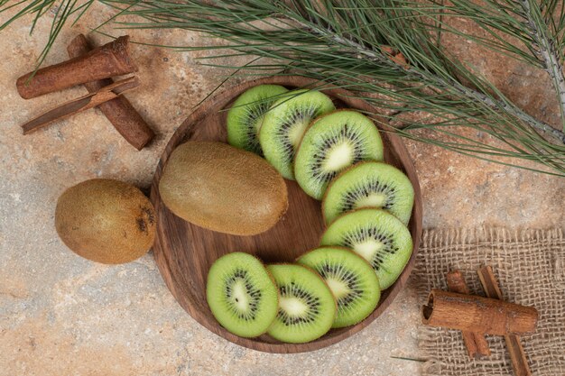 Plate of fresh kiwi and cinnamon sticks on marble surface.