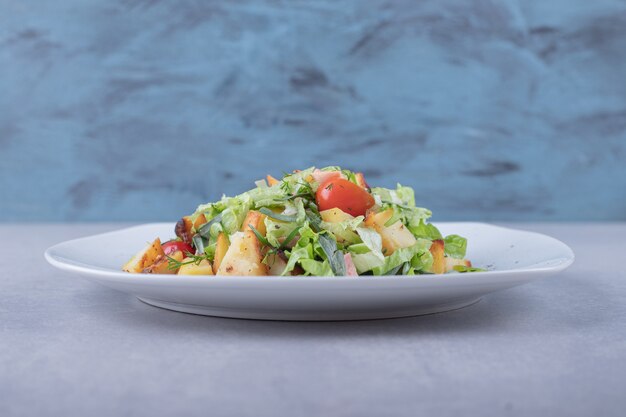 Plate of fresh salad with sausages on stone background.