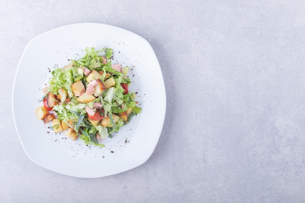 Plate of fresh salad with sausages on stone background. 