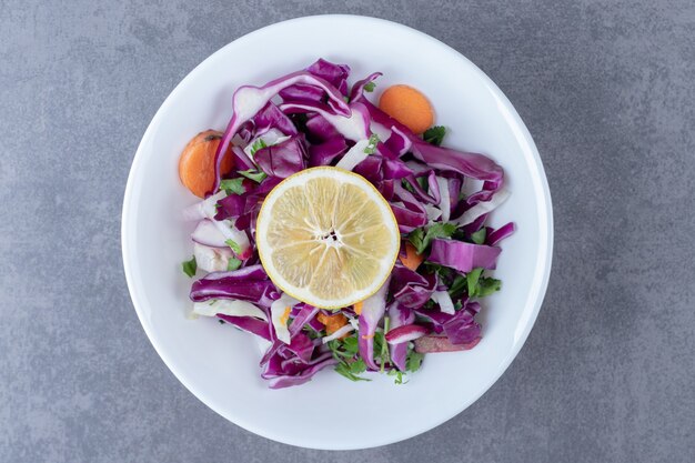 A plate of grated vegetables with lemon , on the marble surface.