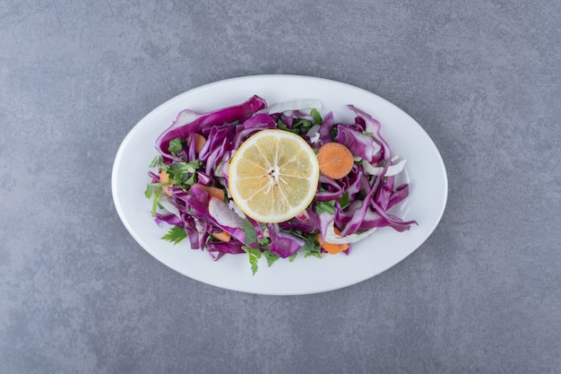 A plate of grated vegetables with lemon , on the marble surface.