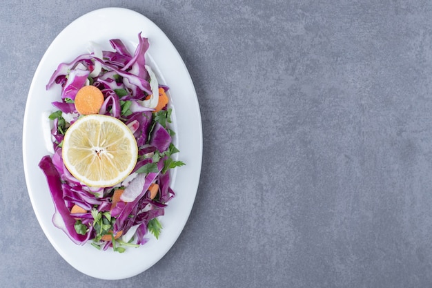 A plate of grated vegetables with lemon , on the marble surface.