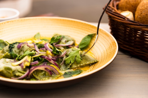 Plate of green ravioli pasta with onion and coriander leaves