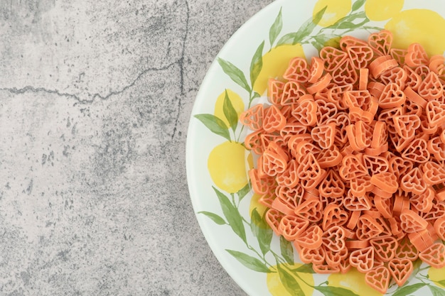 Free photo plate of heart shaped raw macaroni placed on marble background