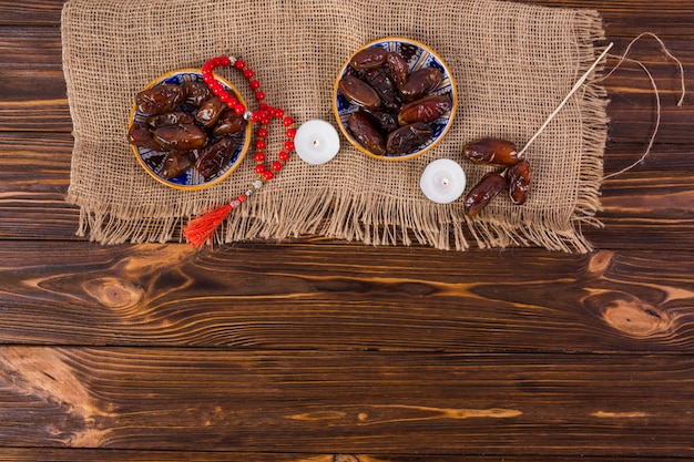 Free photo plate of juicy dates with red prayer beads and lighted candle on wooden desk