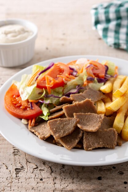 Plate of kebab, vegetables and french fries on wooden table