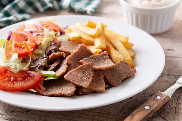 Free photo plate of kebab, vegetables and french fries on wooden table