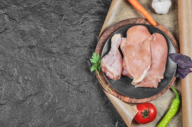 Free photo plate of raw chicken parts with tomato and carrot on dark surface