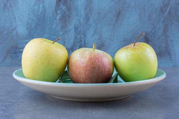 A plate of ripe apples and leaves on the dark surface