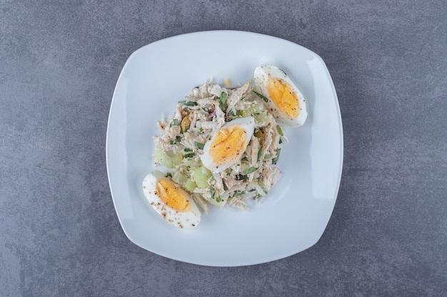 Plate of salad with boiled egg on stone table.