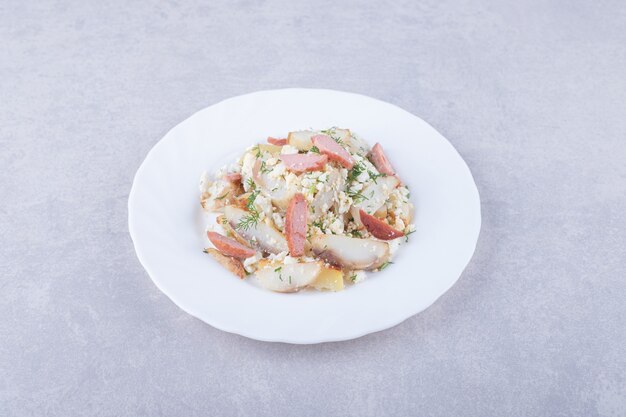 Plate of salad with sausages on stone background. 