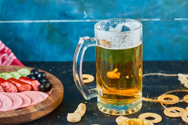 A plate of sausages and a glass of beer on dark table.