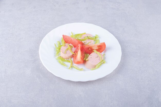 Plate of sliced sausages and tomatoes on stone background. 