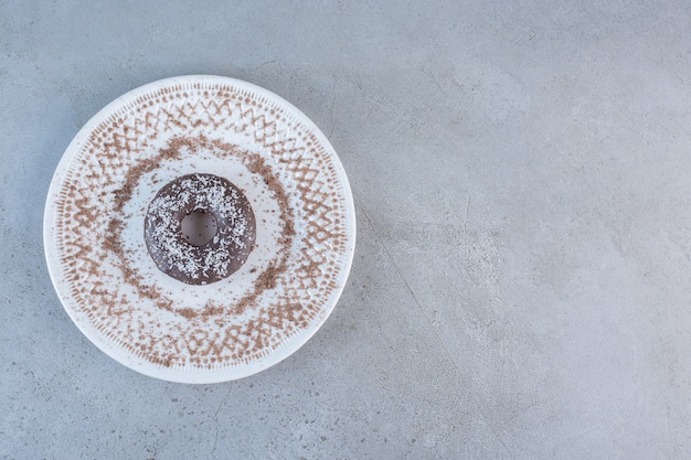 Plate of tasty single chocolate donut on stone.