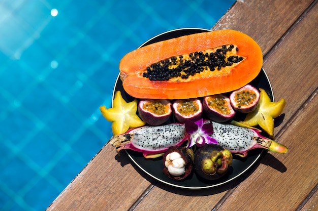 Free photo plate of tasty sweet tropical exotic fruits stay near pool at luxury hotel, papaya, dragon fruit, mangosteen.