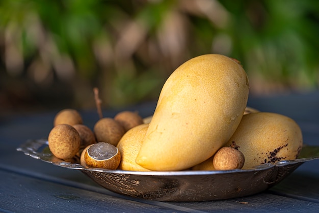 A plate of tropical fruits on a wooden table. Yellow mango and lychee on blurred background.