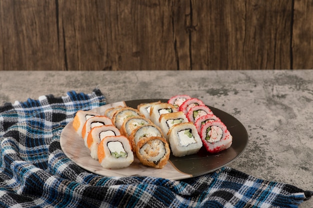 Plate of various delicious sushi rolls on marble table