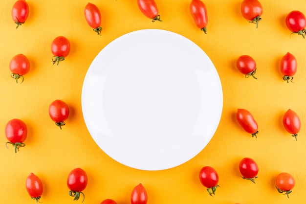 plate with copy space surrounded by red fresh cherry tomatoes on yellow