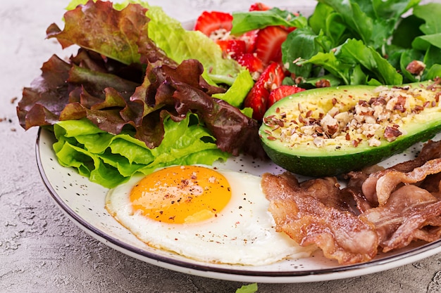 Free Photo plate with a keto diet food. fried egg, bacon, avocado, arugula and strawberries. keto breakfast.