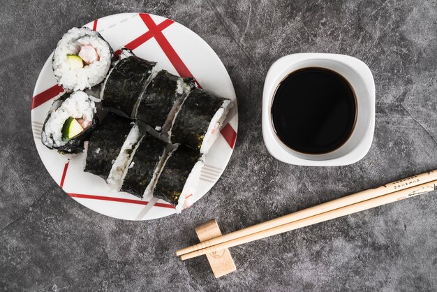 Plate with sushi rolls near soy sauce and chopsticks