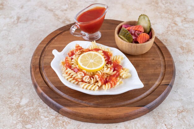 Platter of cooked pasta, ketchup and a bowl mixed pickles on marble surface