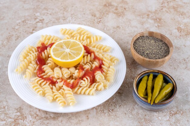 Platter of macaroni with small bowls of black pepper and pickled peppers on marble surface