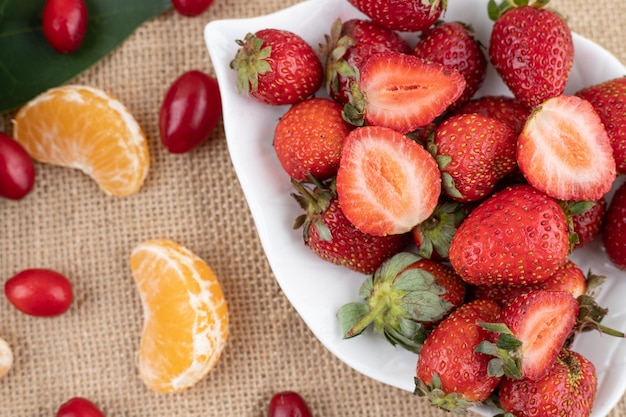 A platter of strawberries and a handful of tangerine slices and hips on textile background. High quality photo