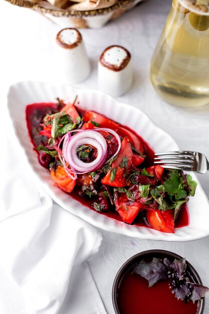 A platter of tomato salad with red onion dark leaves basil coriander dill