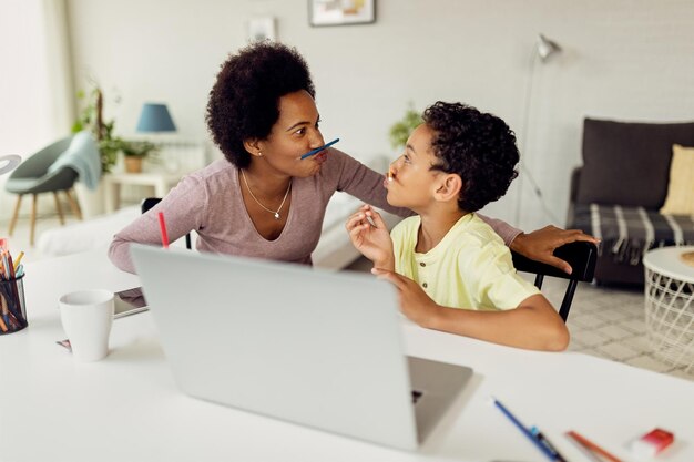 Playful black mother and son having fun while homeschooling