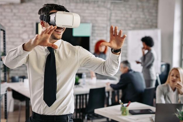 Playful businessman wearing virtual reality headset and having fun in the office There are people in the background