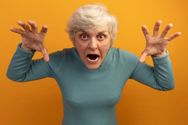 Free Photo playful old woman wearing blue turtleneck sweater doing tiger roar and paws gesture 