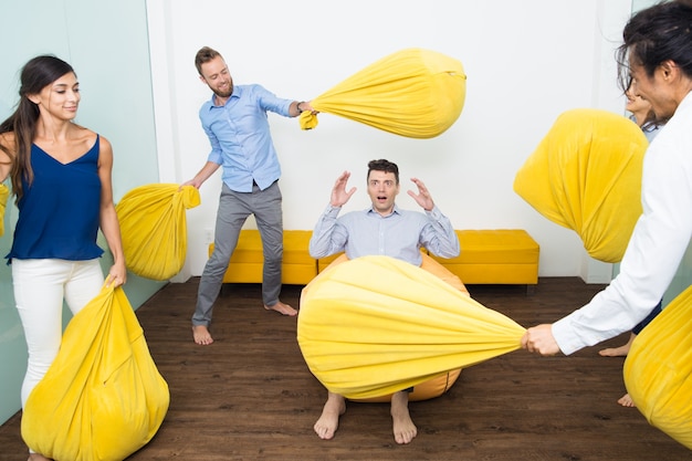 Free photo playful people beating their friend with pillows