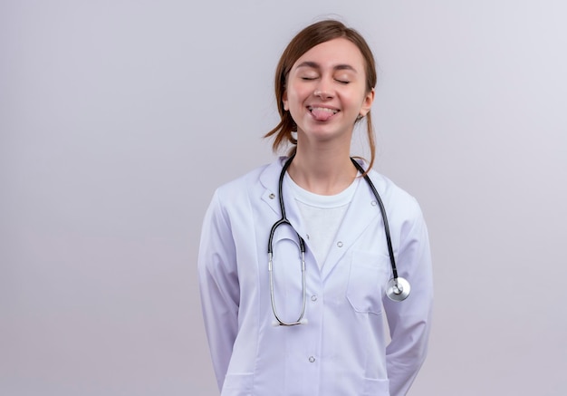 Free photo playful young female doctor wearing medical robe and stethoscope showing tongue with closed eyes  with copy space