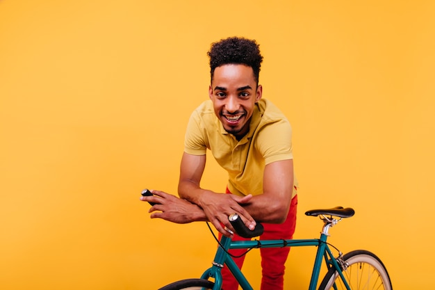 Free Photo pleasant african man with curly hair standing beside bicycle. indoor shot of ecstatic black guy posing