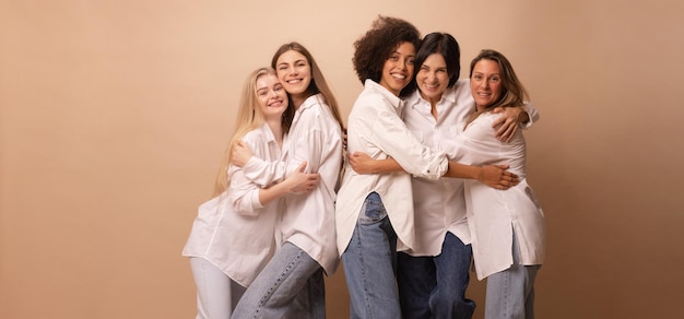 Free Photo pleasant five diverse young and adult ladies in casual wear hugging smiling at camera on brown background