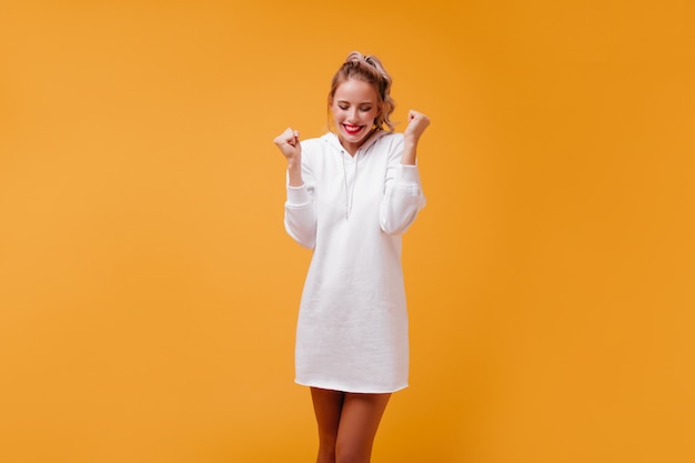 Pleasant, friendly blonde in street-style dress holds her hands in fists and laughs