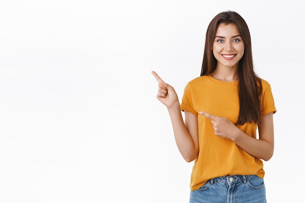 Pleasant friendlylooking pretty caucasian woman in yellow tshirt pointing upper left corner help customer find way recommend product or event promo standing white background confident