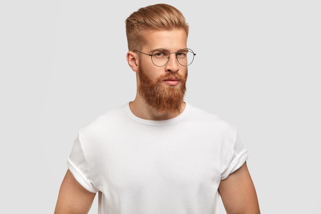 Pleasant looking serious man stands in profile, has confident expression, wears casual white t shirt