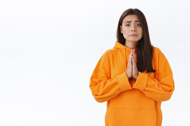 Please I beg you Miserable and hopeful cute sad cute woman asking for help hold hands in pray and frowning uneasy need something asap begging and pleading stand white background