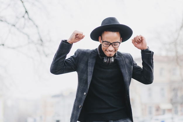 Pleased african man with gently smile posing with hands up. Outdoor portrait of happy black male model wears trendy suit.