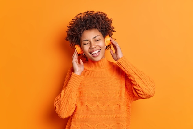 Free Photo pleased afro american woman enjoys pleasant song via stereo headphones smiles broadly keeps eyes closed has happy expression