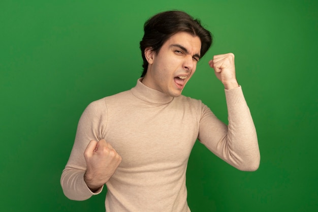 Pleased blinked young handsome guy showing yes gesture isolated on green wall