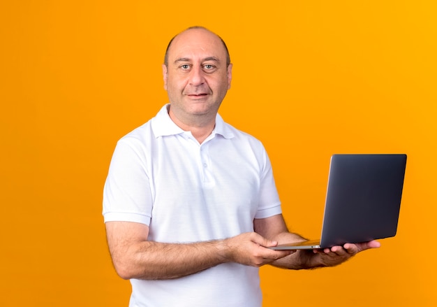 Pleased casual mature man holding laptop isolated on yellow backgound