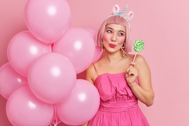 Free photo pleased dreamy woman with pink hair holds green round candy on stick likes sweet lollipops